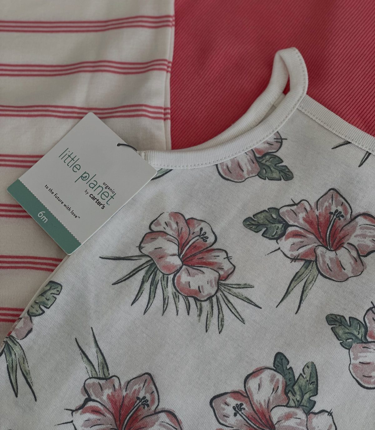 White infant clothes with hibiscus prints and red stripes featuring a Little Planet tag.