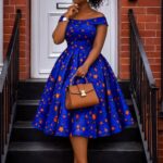 Woman in a blue and orange patterned African print dress holding a brown handbag.