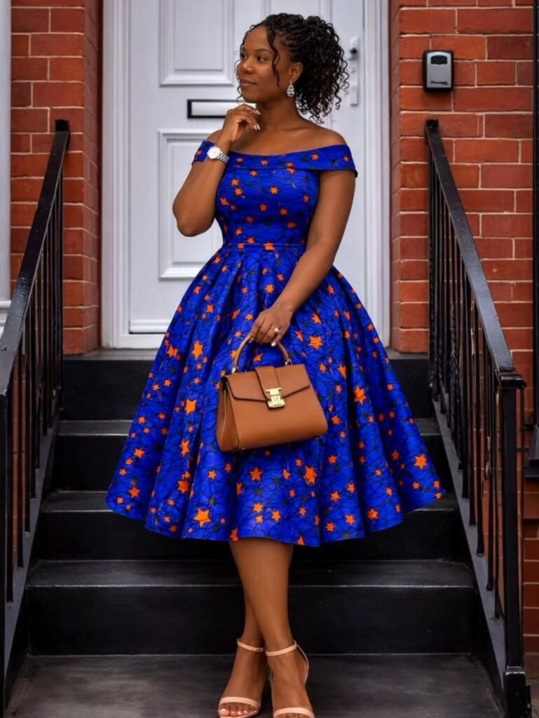 Woman in a blue and orange patterned African print dress holding a brown handbag.