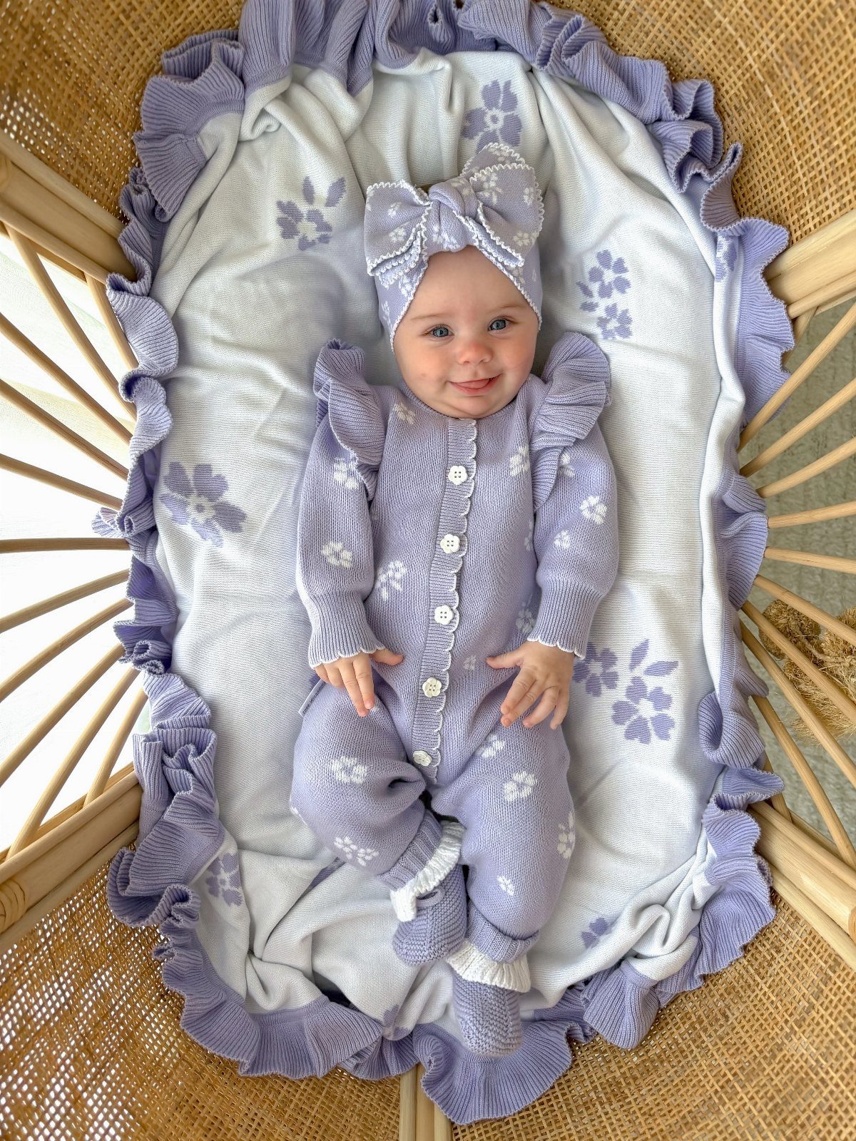 Newborn baby in purple ruffled knitted romper and headband lying in a bassinet