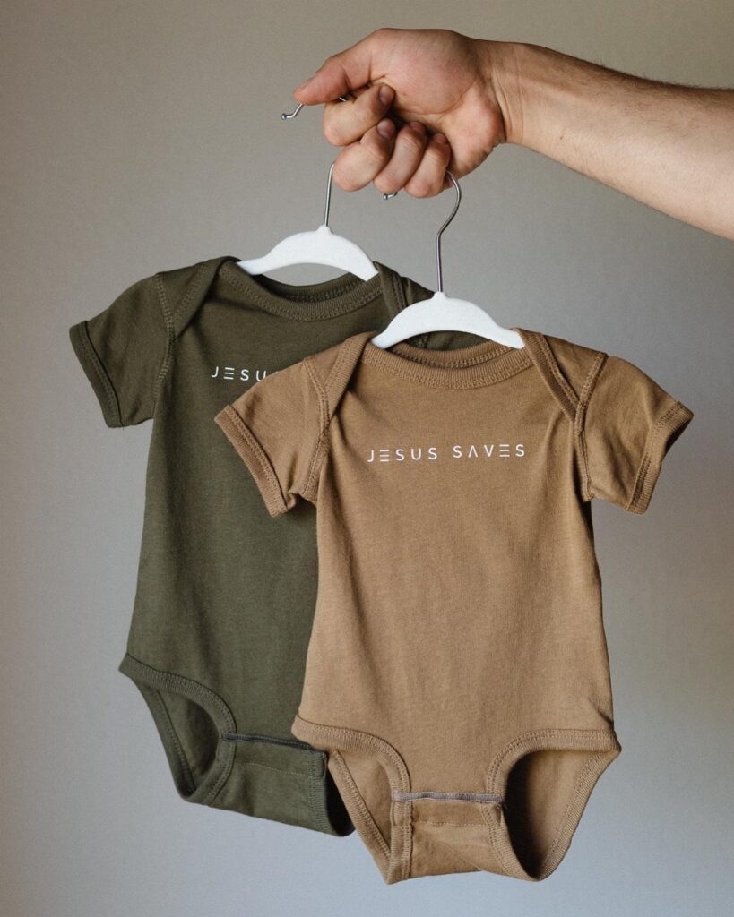 Two baby bodysuits in olive and tan with Jesus Saves printed on them.