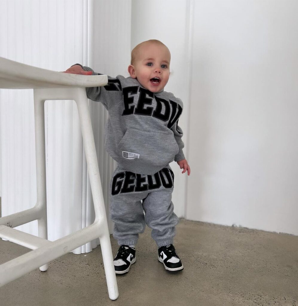 Baby in grey streetwear hoodie and joggers with black and white sneakers.
