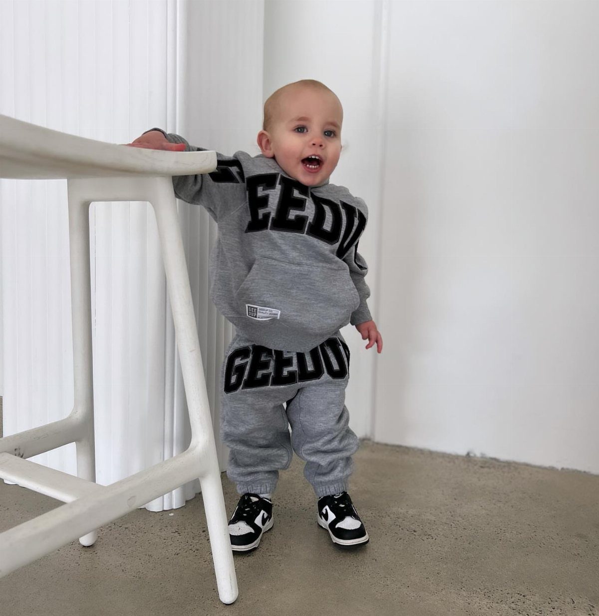 Baby in grey streetwear hoodie and joggers with black and white sneakers.