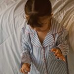 Young child wearing blue and white striped pajamas with red piping on white bedding