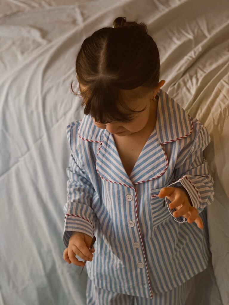 Young child wearing blue and white striped pajamas with red piping on white bedding