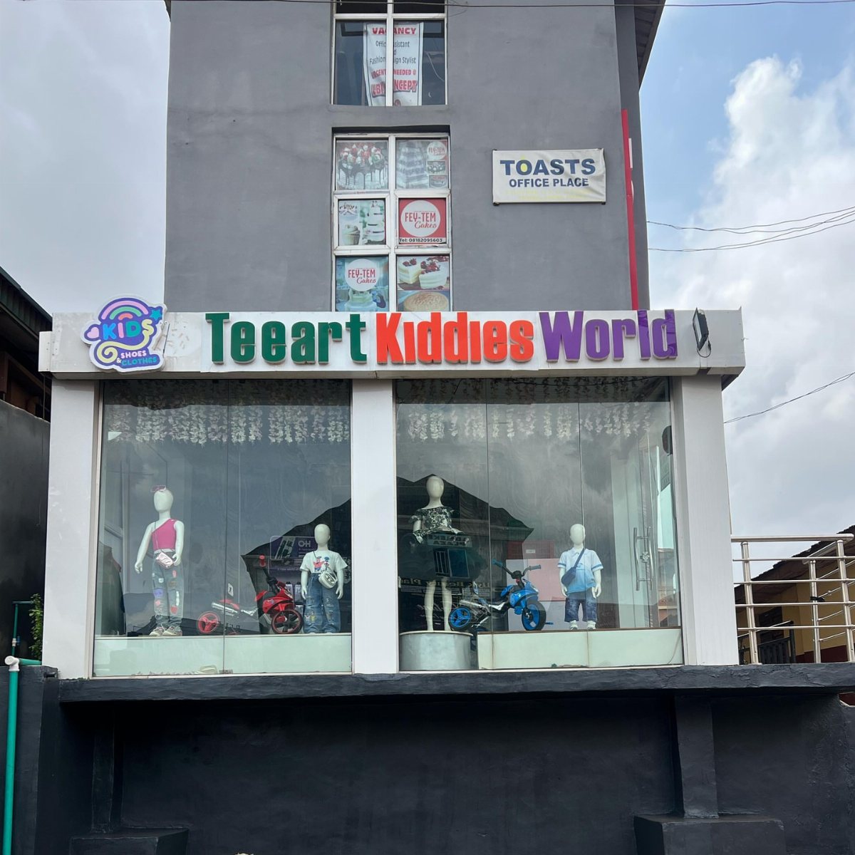 Teeart Kiddies World storefront with child mannequins in clothing and toy motorcycles.