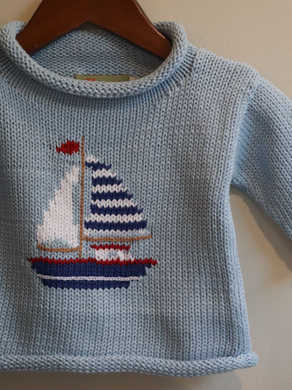 Light blue knitted infant sweater with an embroidered sailboat on the front.