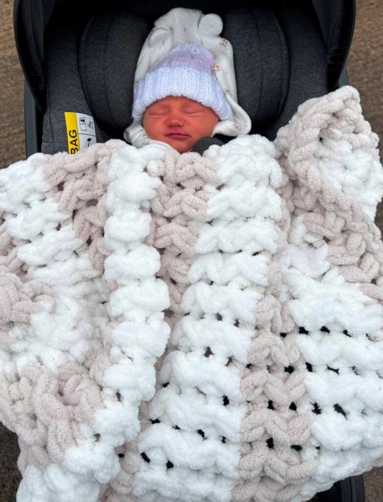 Sleeping newborn in a stroller covered by a chunky white and beige knit blanket