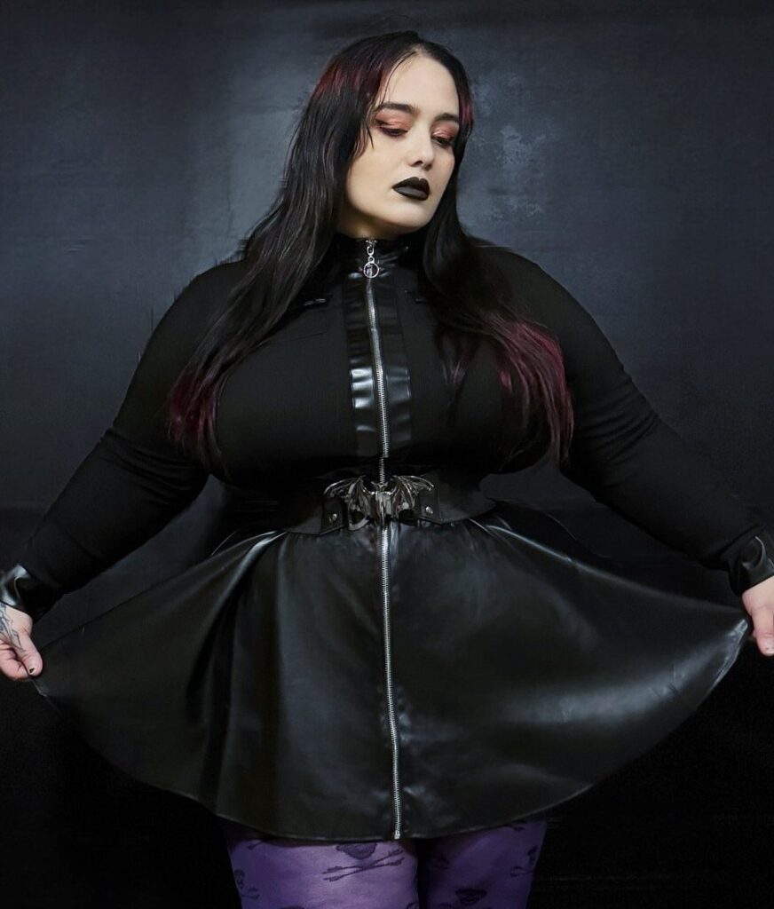 Plus-size woman wearing a black gothic outfit with a faux-leather zipper skirt.