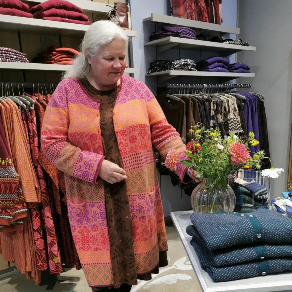 Woman in a patterned orange cardigan standing in a clothing store with flowers.