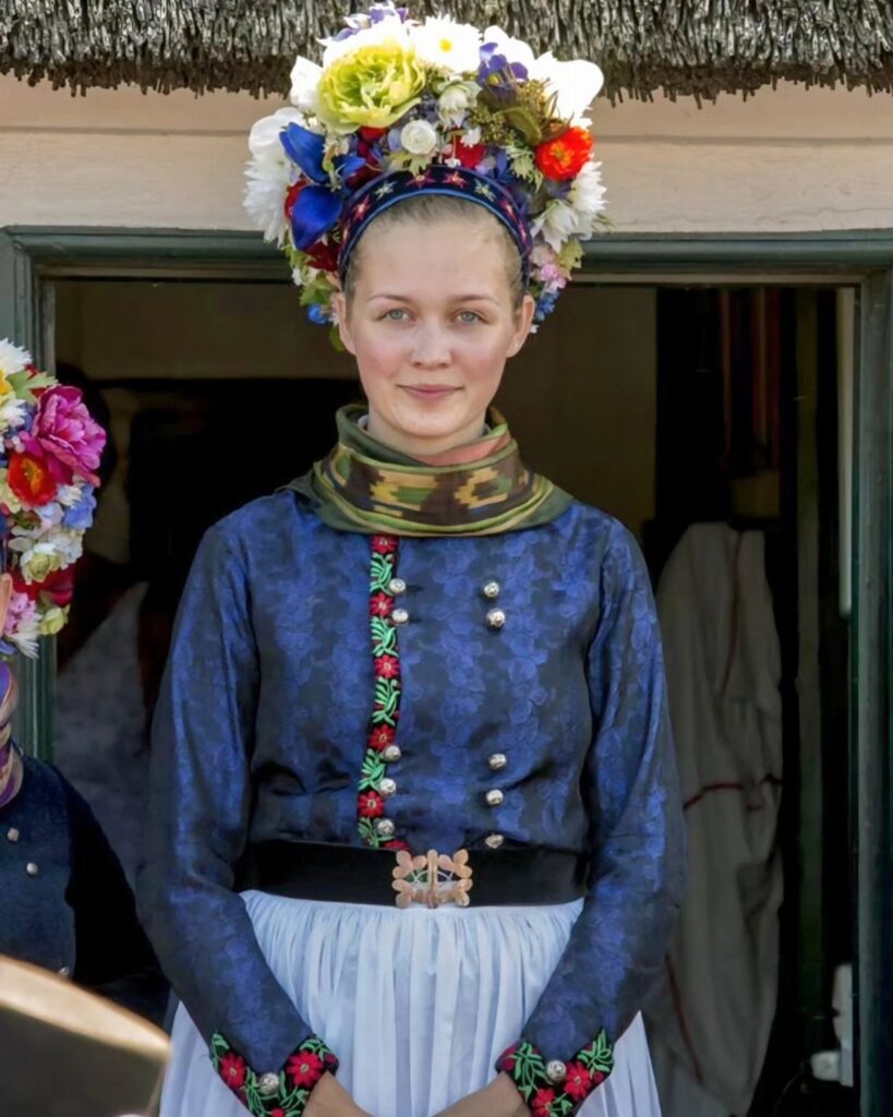 Woman in traditional Danish folk dress with a colorful floral crown and blue bodice.