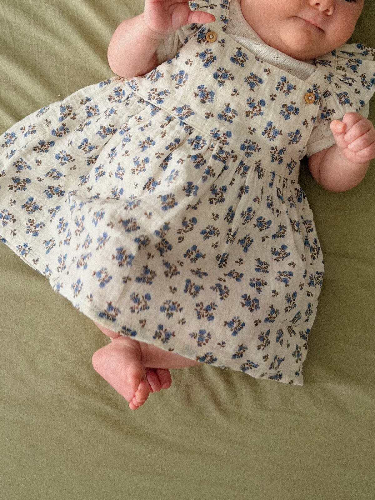 Newborn baby wearing a white dress with blue floral patterns on green fabric.